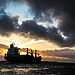 Cargo ship sailing under dark clouds at sunset