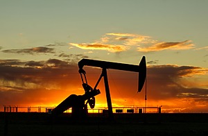 An onshore oil pump jack against a vibrant sunset sky. 