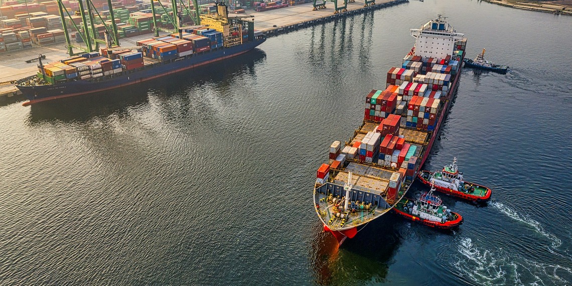 Three pilot boats push a large cargo ship into the dock.