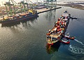 Three pilot boats push a large cargo ship into the dock.
