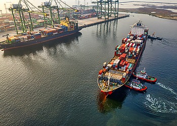 Three pilot boats push a large cargo ship into the dock.