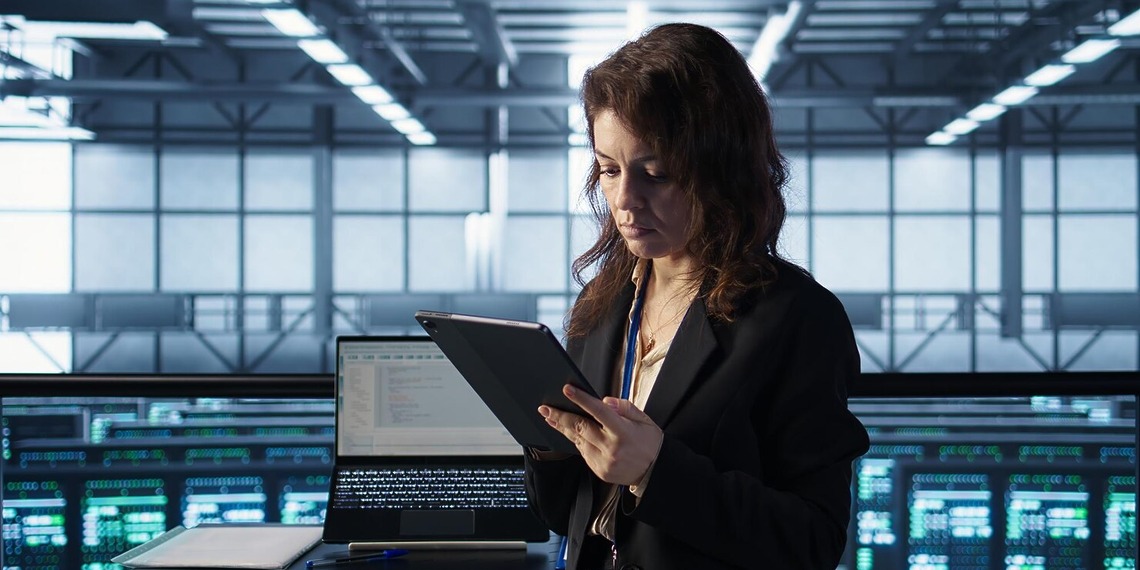 Compliance professional using a tablet beside digital monitoring dashboards