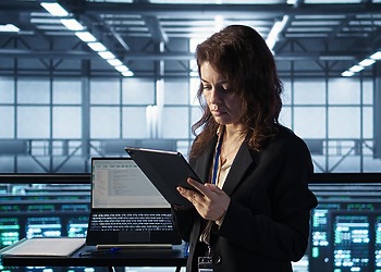 Compliance professional using a tablet beside digital monitoring dashboards