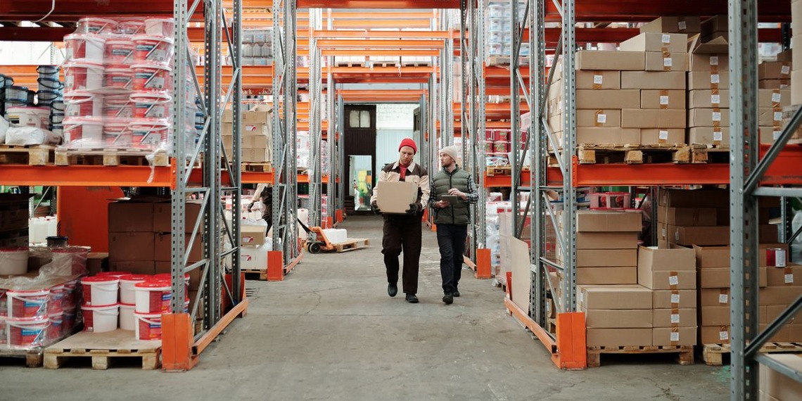 Two warehouse workers handling a package between storage racks