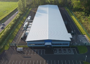 Aerial view of a large white data centre with pitched roof next to a road.