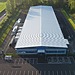 Aerial view of a large white data centre with pitched roof next to a road.