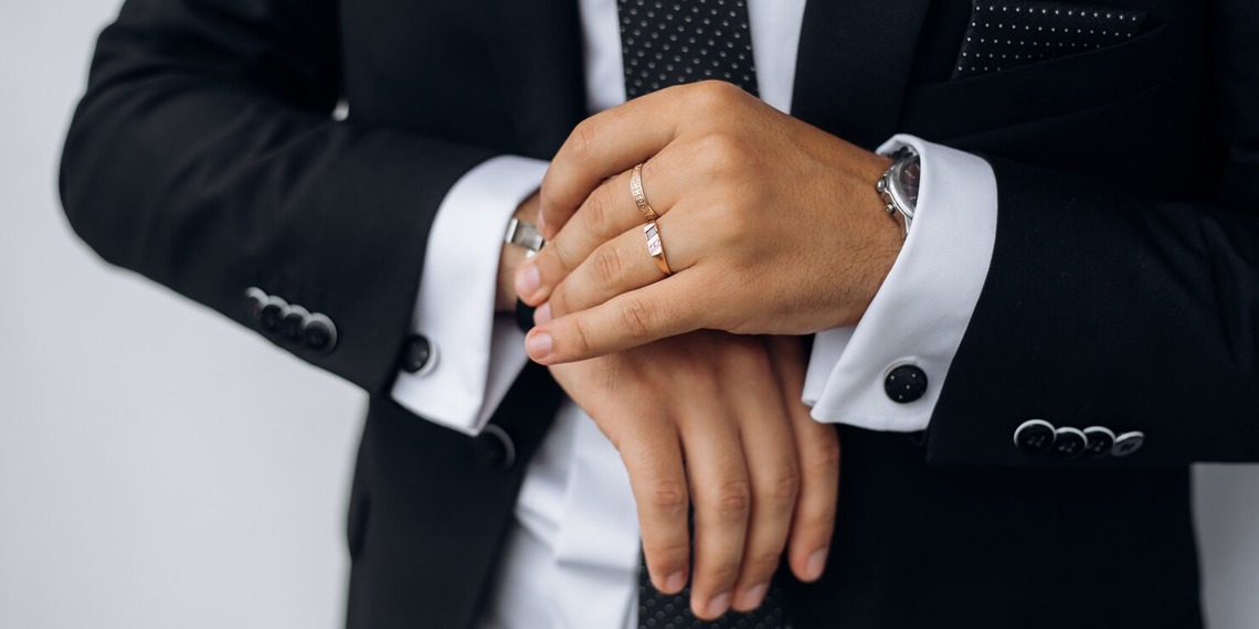 Man in a dark suit wearing a wedding band