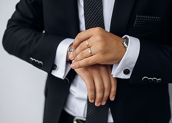 Man in a dark suit wearing a wedding band