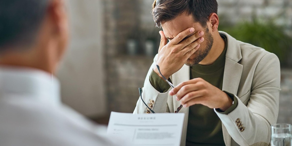 Man holding his head during a consultation across a desk