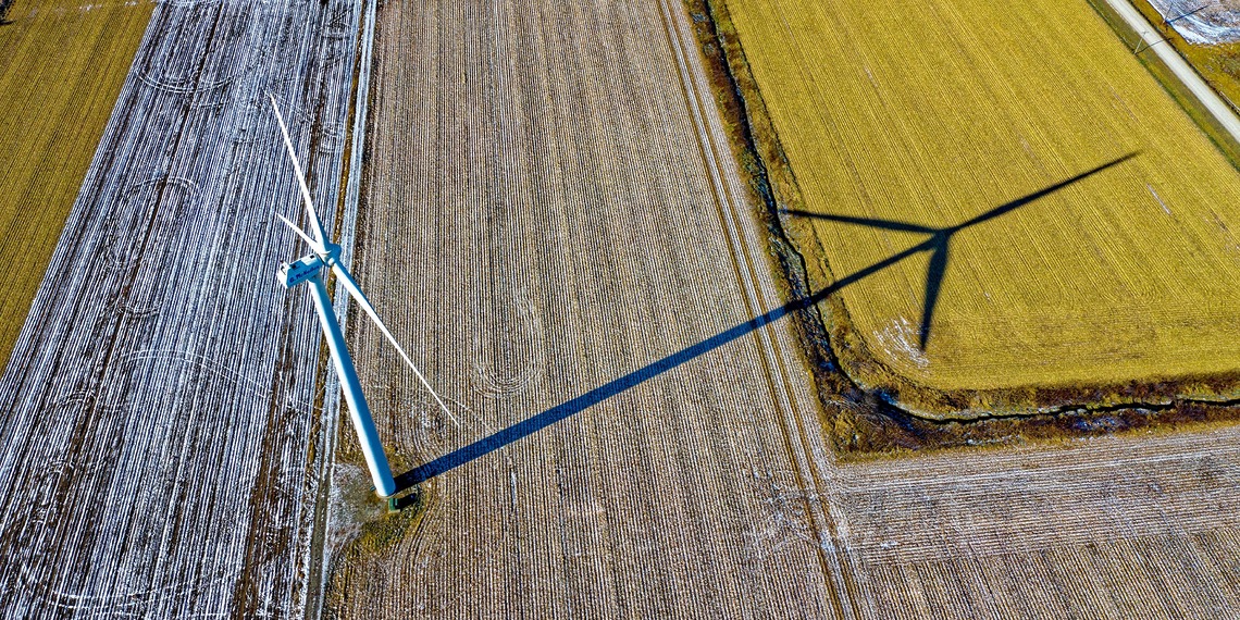 Wind turbine casting a shadow on farmland.