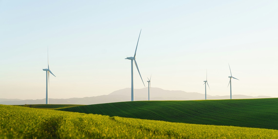 Wind turbines rising above a grassy field under an open sky