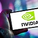 Close-up of a hand holding a smartphone showing the NVIDIA logo on screen with a blurred background.
