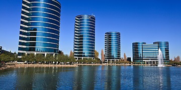 Four round corporate buildings viewed across a body of water.
