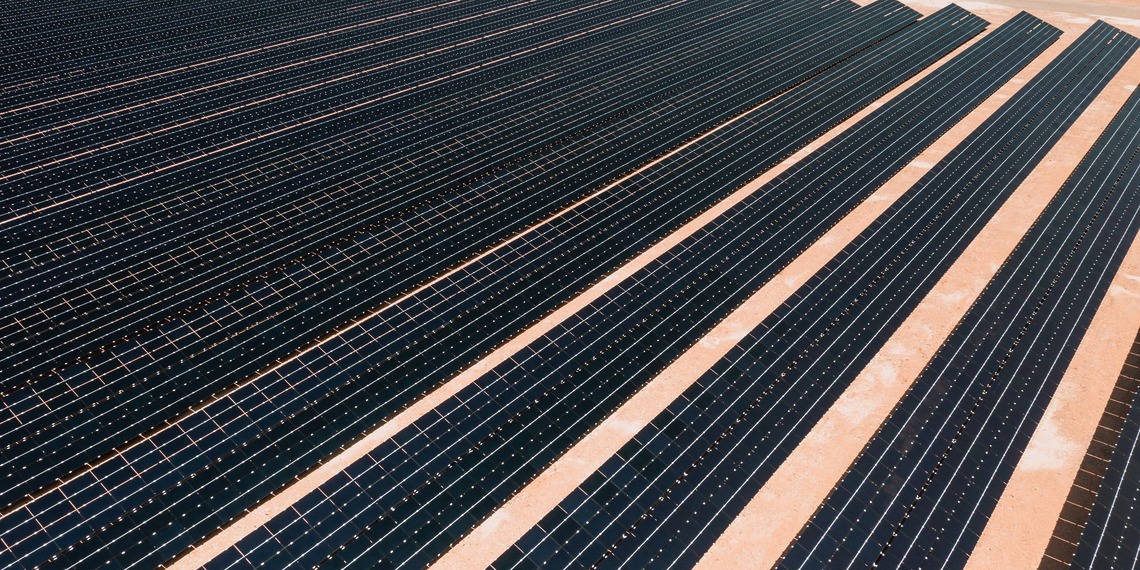 Aerial view of solar panels in a vast solar farm under bright sunlight.