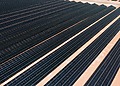 Aerial view of solar panels in a vast solar farm under bright sunlight.