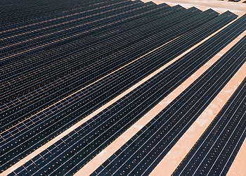 Aerial view of solar panels in a vast solar farm under bright sunlight.