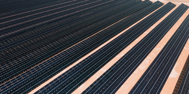 Aerial view of solar panels in a vast solar farm under bright sunlight.