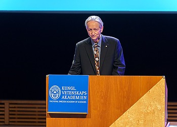 Geoffrey Hinton behind a speaker’s platform, accepting the Nobel Prize in 2024