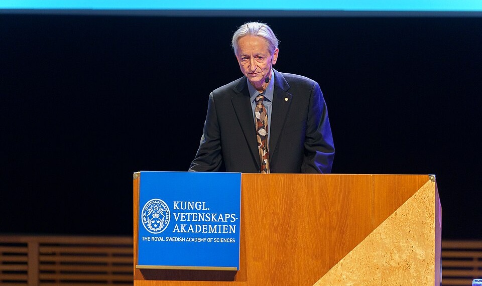 Geoffrey Hinton behind a speaker’s platform, accepting the Nobel Prize in 2024