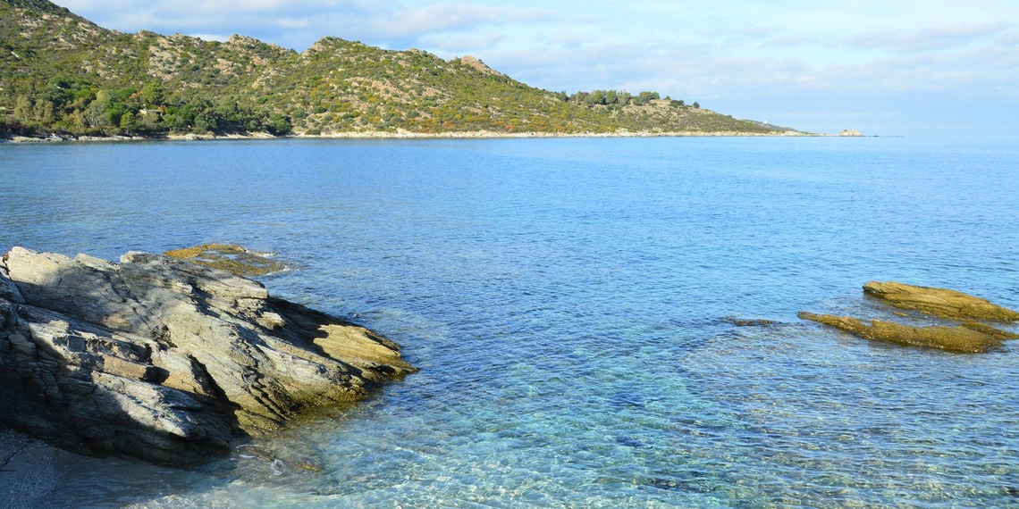 Clear blue water and rocky shoreline at Patrimonio, Corsica, on the Mediterranean coast.