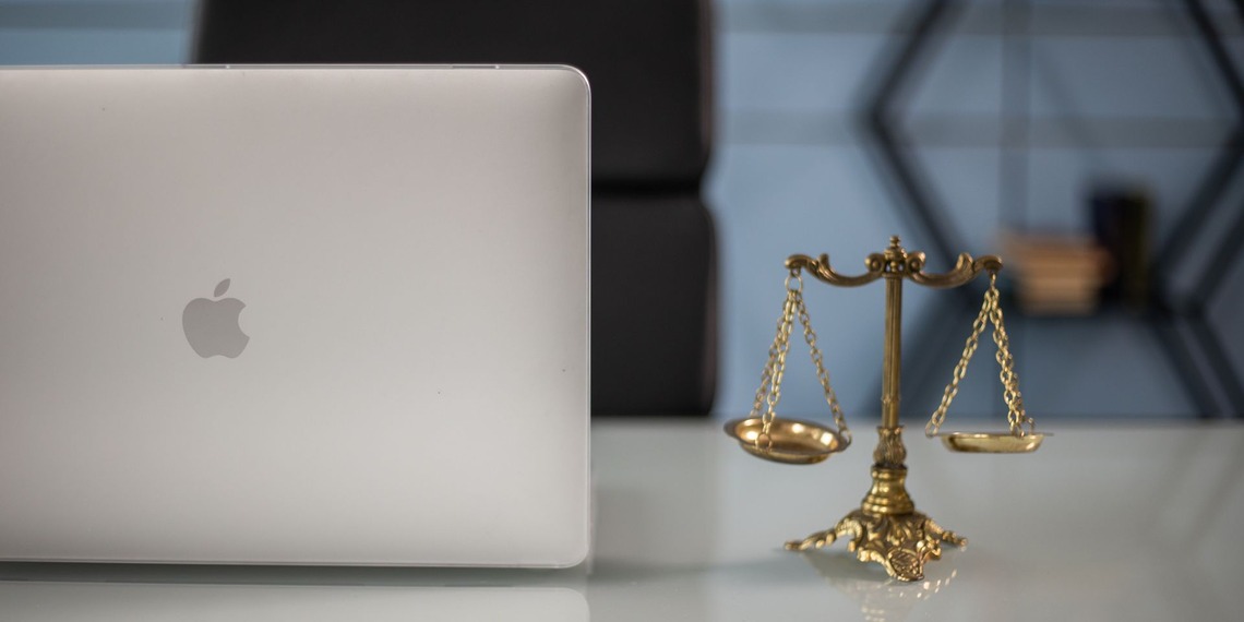 Justice scales and a silver Apple laptop sit on a desk at a law office.