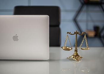 Justice scales and a silver Apple laptop sit on a desk at a law office.