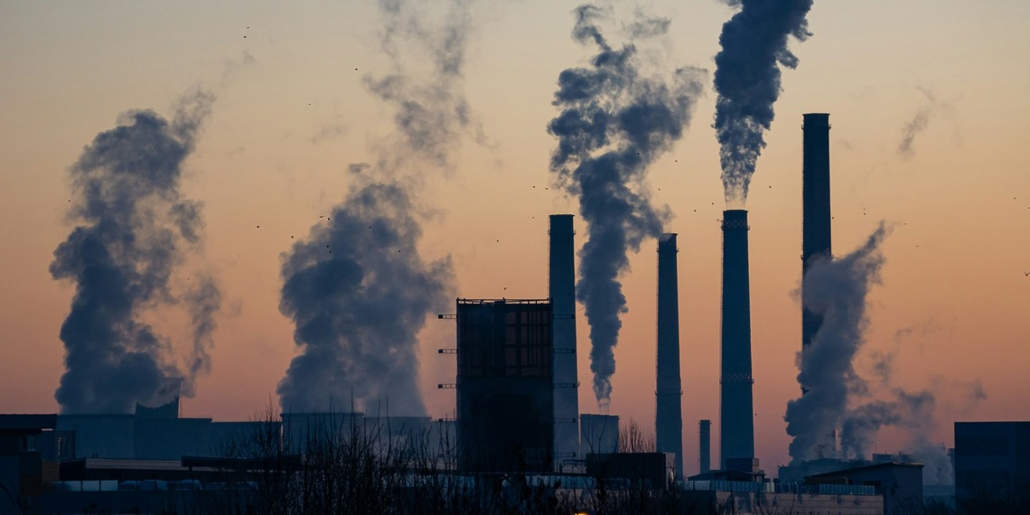 Silhouetted power plant smokestacks emitting smoke at sunset