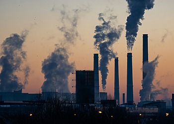 Silhouetted power plant smokestacks emitting smoke at sunset