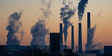 Silhouetted power plant smokestacks emitting smoke at sunset