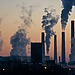 Silhouetted power plant smokestacks emitting smoke at sunset