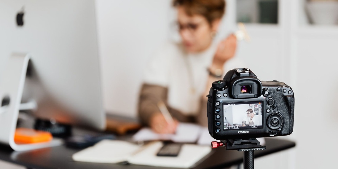 Woman in an office using a camera to create content, showcasing modern technology and creativity.