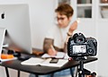 Woman in an office using a camera to create content, showcasing modern technology and creativity.