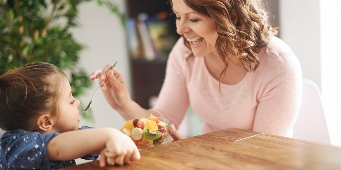 Woman offering food to a young child seated at a table