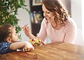Woman offering food to a young child seated at a table