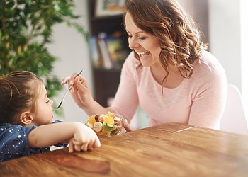 Woman offering food to a young child seated at a table