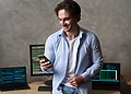 Software developer holding a smartphone in front of multiple coding screens