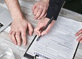 Close-up image of two people signing an insurance policy document on a wooden desk.