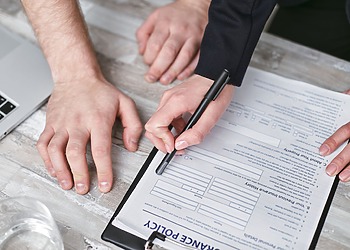 Close-up image of two people signing an insurance policy document on a wooden desk.