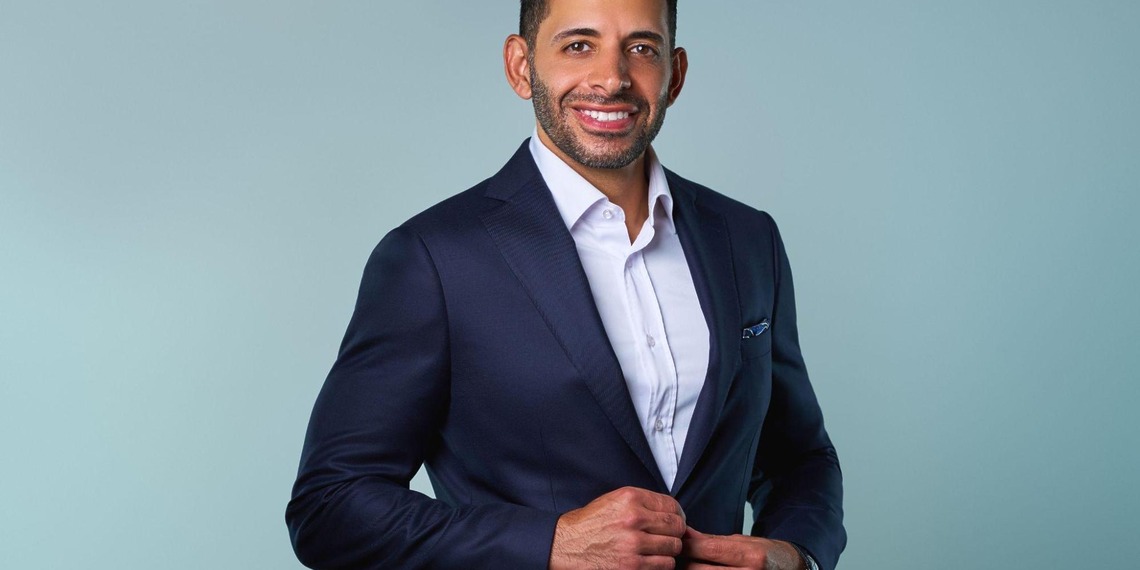 Man in a navy suit smiling against a light blue background