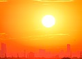 A bright orange sky with the sun over a city silhouette.