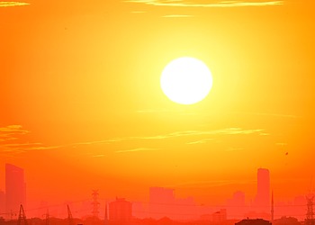 A bright orange sky with the sun over a city silhouette.