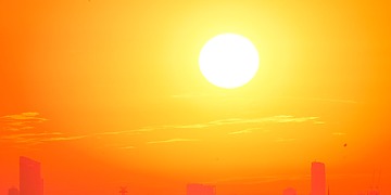 A bright orange sky with the sun over a city silhouette.
