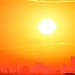 A bright orange sky with the sun over a city silhouette.