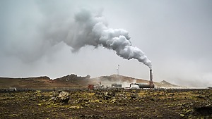 Derelict landscape with large white plume of smoke emerging from a small smokestack.