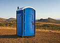 Blue portable toilet standing in a dry rural landscape