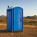 Blue portable toilet standing in a dry rural landscape