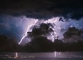 Lightning strikes over a coastal city at night.