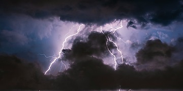 Lightning strikes over a coastal city at night.