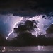 Lightning strikes over a coastal city at night.