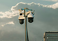 Multiple surveillance cameras mounted on a pole against a cloudy sky